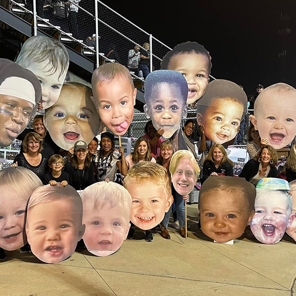 Football moms holding up BigHeads cutouts.